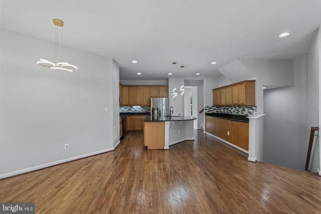 23466 Twin Falls Ter, Brambleton, VA 20148 - kitchen featuring stainless steel fridge with ice dispenser, dark countertops, decorative backsplash, dark wood-style flooring, and a center island with sink