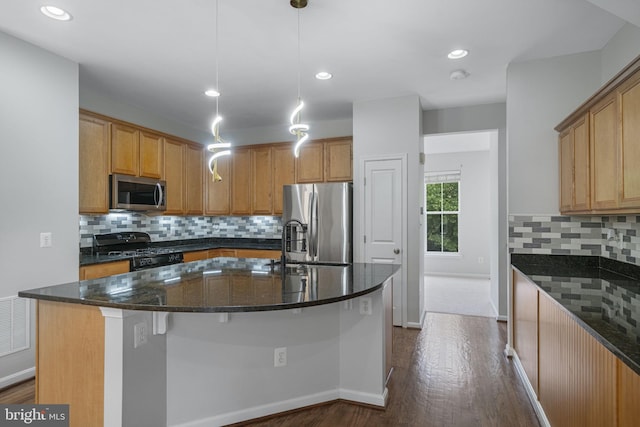 23466 Twin Falls Ter, Brambleton, VA 20148 - kitchen featuring appliances with stainless steel finishes, dark wood-style floors, a center island with sink, dark stone countertops, and decorative backsplash