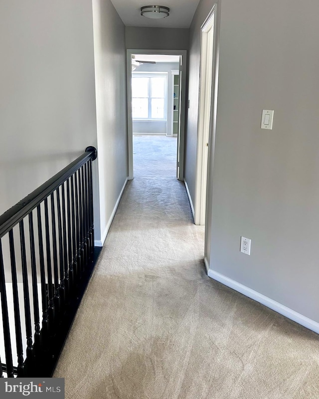 hallway featuring carpet floors, baseboards, and an upstairs landing