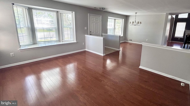 unfurnished living room featuring a chandelier, dark wood-style flooring, and baseboards