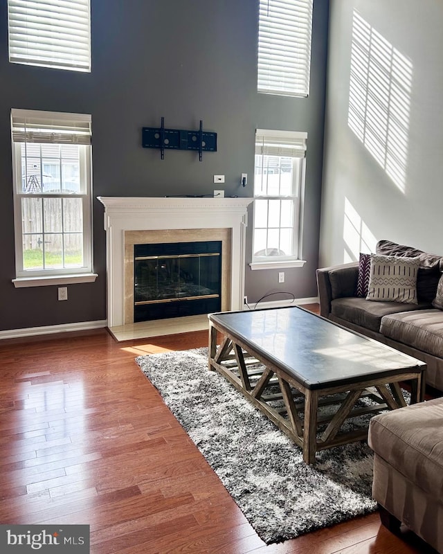 living room with a fireplace with flush hearth, healthy amount of natural light, wood finished floors, baseboards, and a towering ceiling