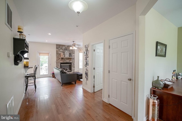 living room featuring wood finished floors, a ceiling fan, a fireplace, and baseboards