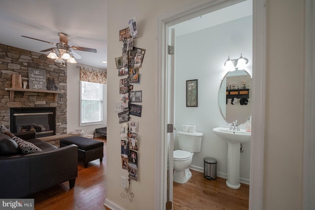 bathroom with a ceiling fan, wood finished floors, toilet, and a fireplace