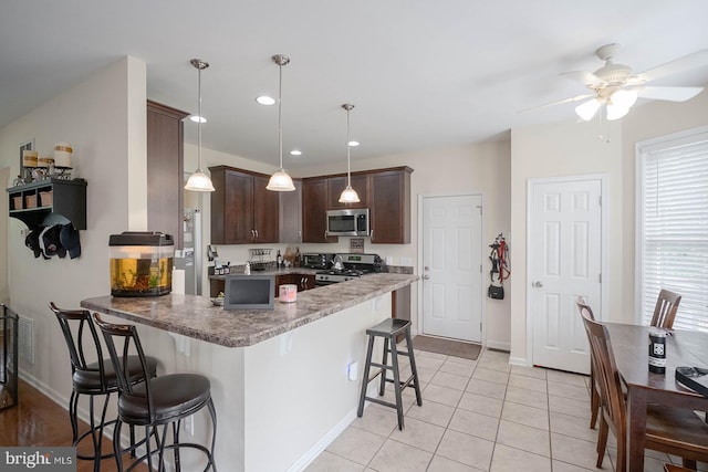 kitchen with stainless steel appliances, dark brown cabinets, a peninsula, a kitchen bar, and ceiling fan