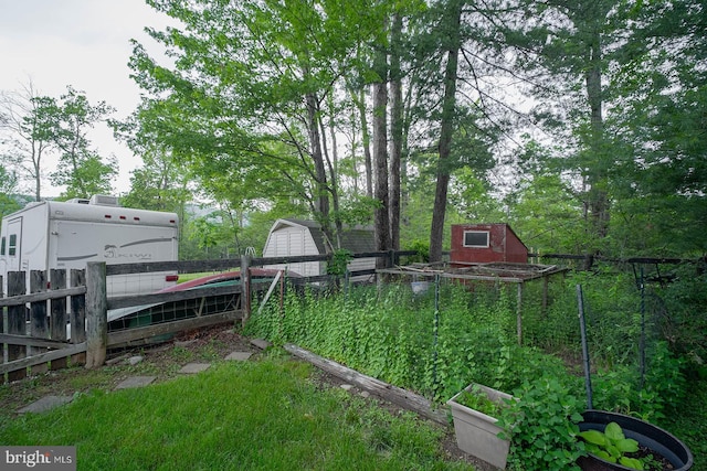 view of yard featuring a vegetable garden, fence, a storage unit, and an outdoor structure