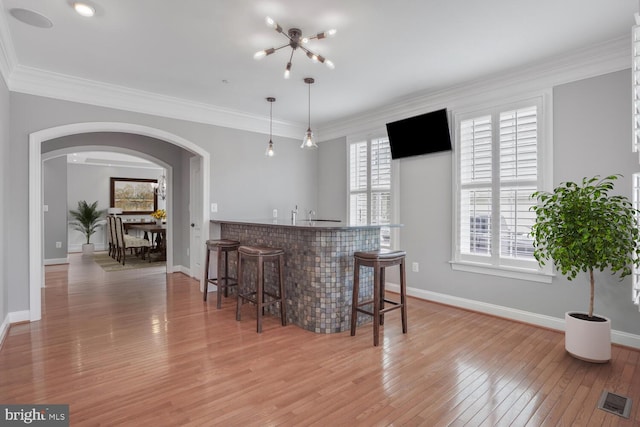 indoor wet bar featuring arched walkways, light wood-type flooring, baseboards, hanging light fixtures, and ornamental molding