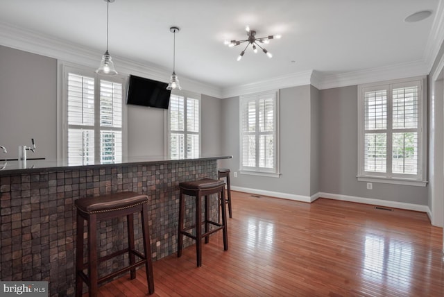 kitchen featuring baseboards, hardwood / wood-style flooring, a breakfast bar, hanging light fixtures, and ornamental molding