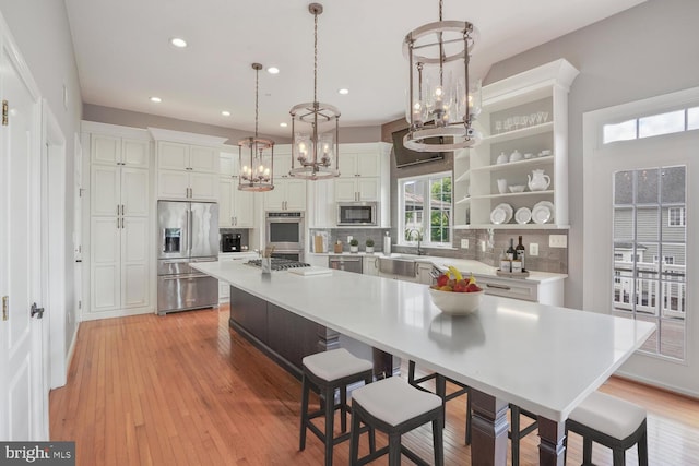 kitchen with stainless steel appliances, a chandelier, a sink, backsplash, and white cabinets
