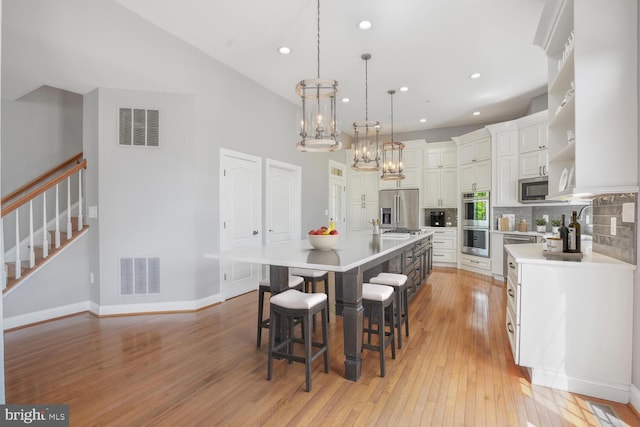 kitchen with appliances with stainless steel finishes, open shelves, light countertops, light wood-style flooring, and a chandelier