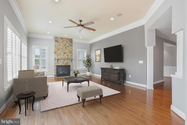 living area with wood finished floors, ceiling fan, a fireplace, crown molding, and baseboards