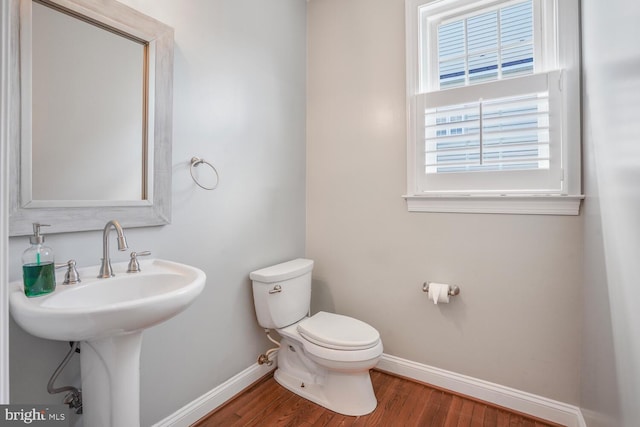 half bath featuring baseboards, wood finished floors, toilet, and a sink