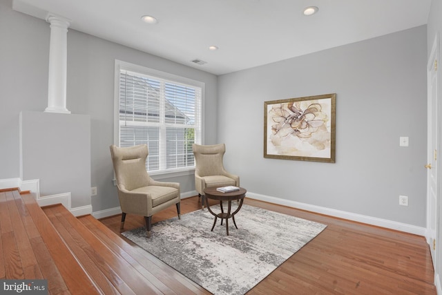 sitting room with wood finished floors, baseboards, recessed lighting, and decorative columns