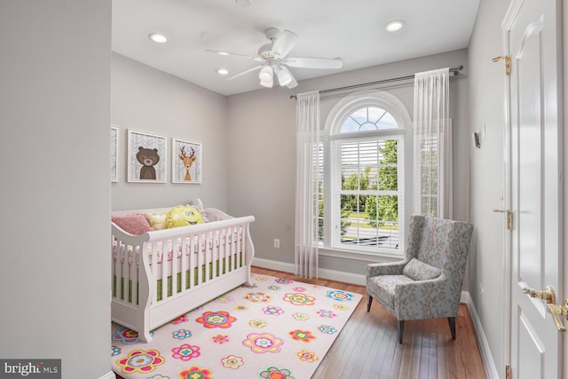 bedroom featuring hardwood / wood-style flooring, baseboards, a crib, recessed lighting, and ceiling fan