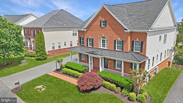 view of front of home with brick siding, a standing seam roof, covered porch, and a front lawn