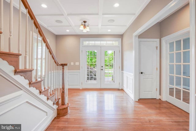 entrance foyer featuring light wood finished floors, healthy amount of natural light, coffered ceiling, stairway, and a wainscoted wall