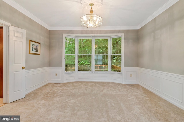 spare room featuring a chandelier, carpet floors, a decorative wall, wainscoting, and ornamental molding