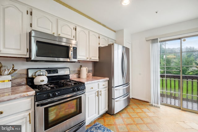 kitchen with appliances with stainless steel finishes, white cabinetry, light floors, and light stone countertops