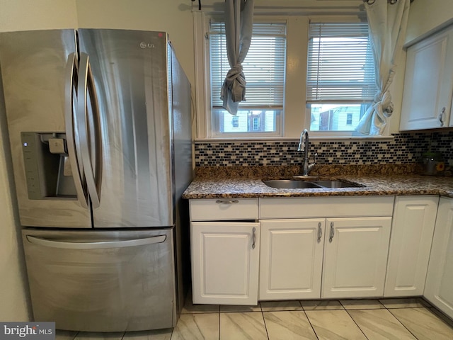 kitchen with stainless steel fridge with ice dispenser, a sink, light tile patterned floors, white cabinetry, and backsplash