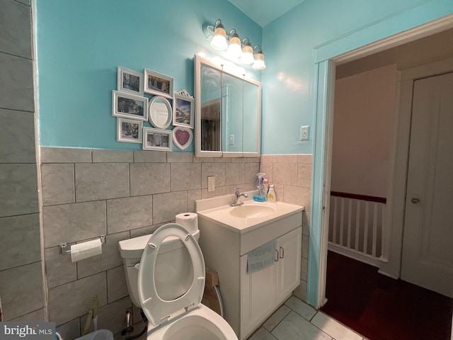bathroom with toilet, tile walls, tile patterned flooring, vanity, and wainscoting