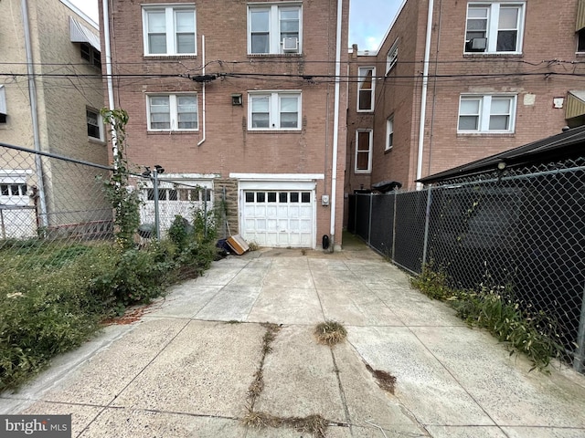 rear view of property with an attached garage, driveway, brick siding, and fence