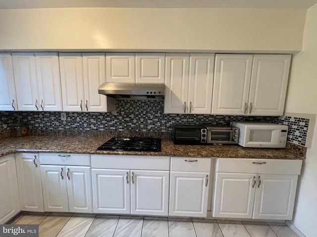kitchen featuring black gas stovetop, white microwave, under cabinet range hood, white cabinets, and decorative backsplash