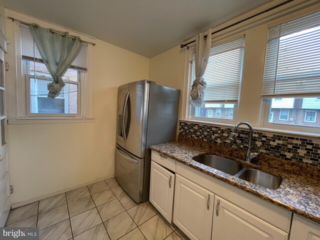 kitchen featuring a sink, stainless steel fridge, dark stone countertops, white cabinetry, and decorative backsplash