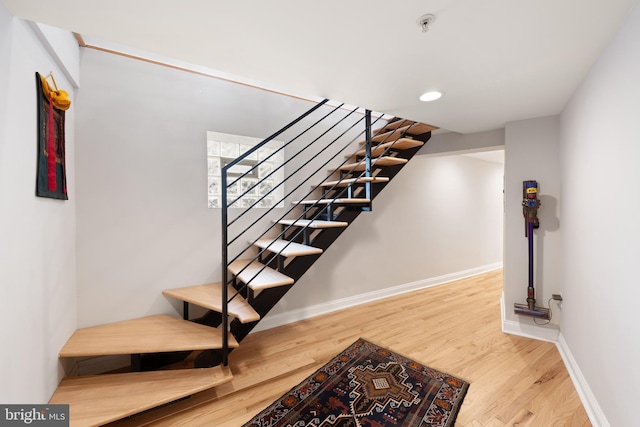 staircase featuring wood finished floors, baseboards, and recessed lighting