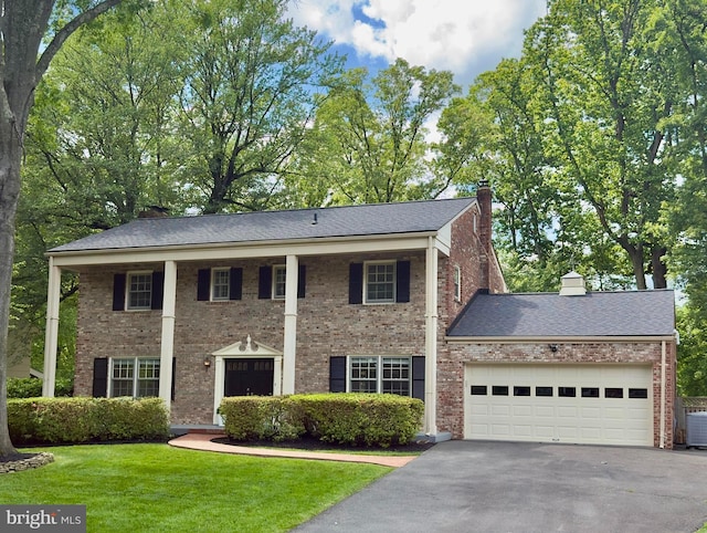 neoclassical home featuring a chimney, driveway, an attached garage, a front yard, and cooling unit