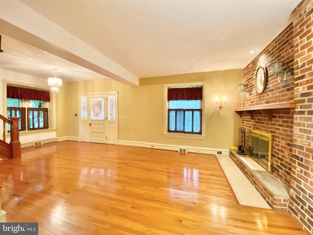 unfurnished living room with hardwood / wood-style flooring, a chandelier, a brick fireplace, baseboards, and plenty of natural light