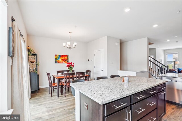 kitchen with dishwasher, light wood finished floors, a chandelier, light stone counters, and a center island