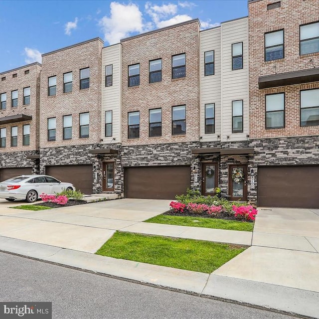 multi unit property featuring an attached garage, driveway, and stone siding