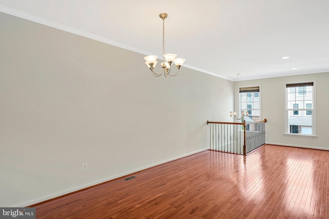 spare room with a chandelier, wood finished floors, ornamental molding, baseboards, and recessed lighting