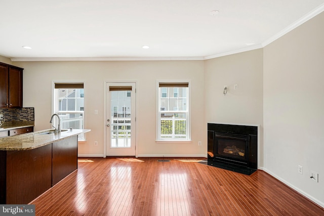 kitchen with ornamental molding, light stone counters, light wood-style floors, dark brown cabinets, and a sink