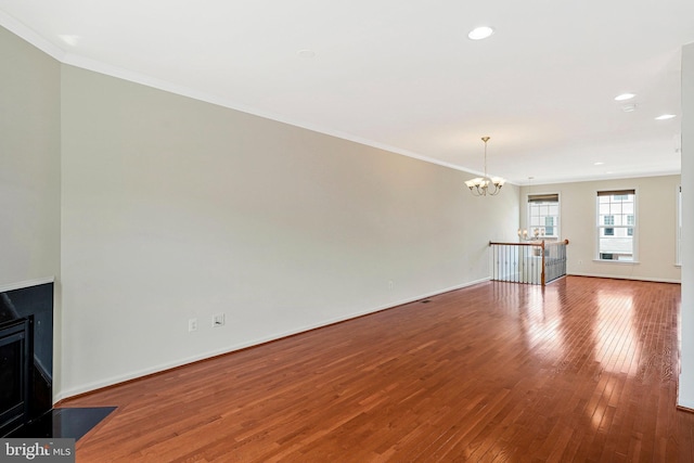 unfurnished living room featuring a chandelier, hardwood / wood-style flooring, ornamental molding, baseboards, and a fireplace with flush hearth