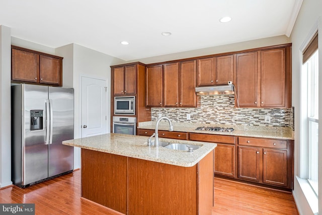 kitchen featuring appliances with stainless steel finishes, a sink, under cabinet range hood, light stone counters, and light wood finished floors