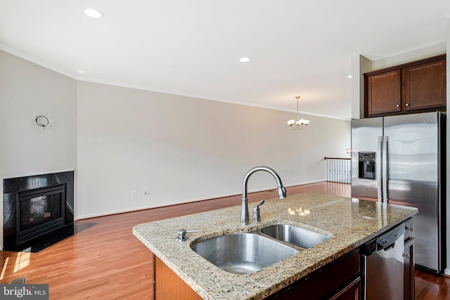 kitchen featuring stainless steel appliances, a sink, crown molding, wood finished floors, and a fireplace with flush hearth