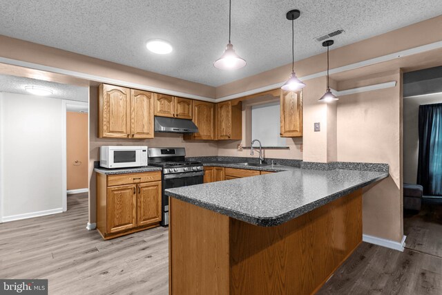 kitchen featuring stainless steel gas range, white microwave, under cabinet range hood, a sink, and dark countertops