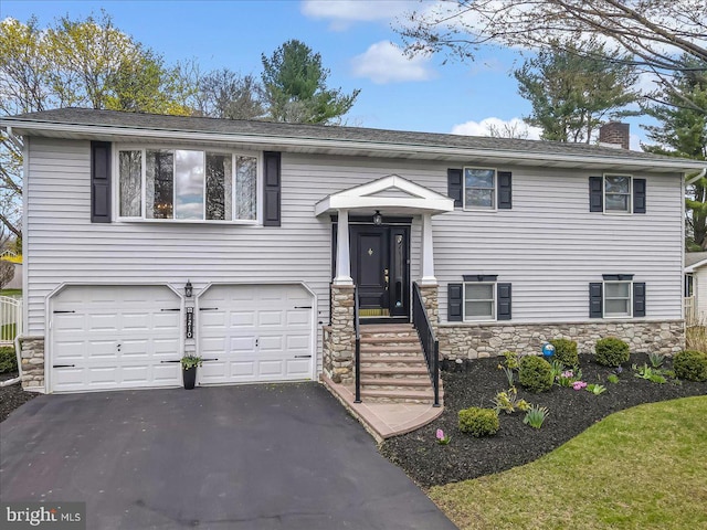 split foyer home featuring stone siding, an attached garage, asphalt driveway, and a chimney
