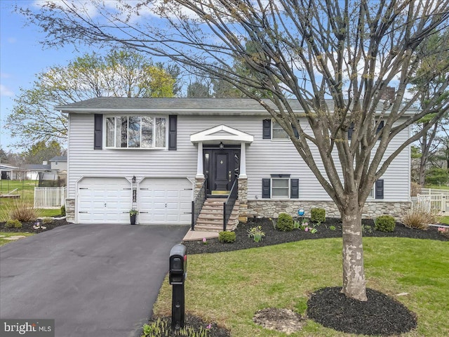 split foyer home with an attached garage, asphalt driveway, stone siding, and a shingled roof