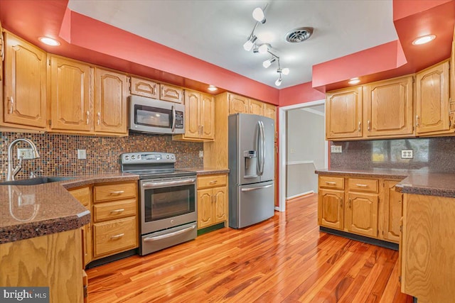 kitchen with stainless steel appliances, a sink, light wood finished floors, and tasteful backsplash