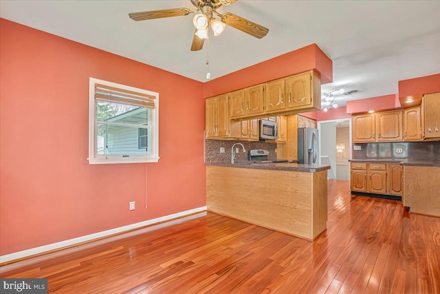 kitchen with appliances with stainless steel finishes, dark countertops, a sink, light wood-style flooring, and a peninsula