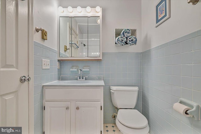bathroom featuring tile walls, toilet, vanity, and wainscoting