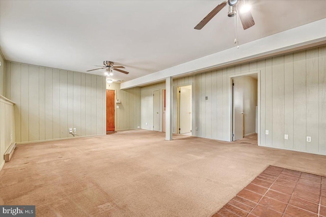unfurnished living room featuring ceiling fan, carpet flooring, and wood walls