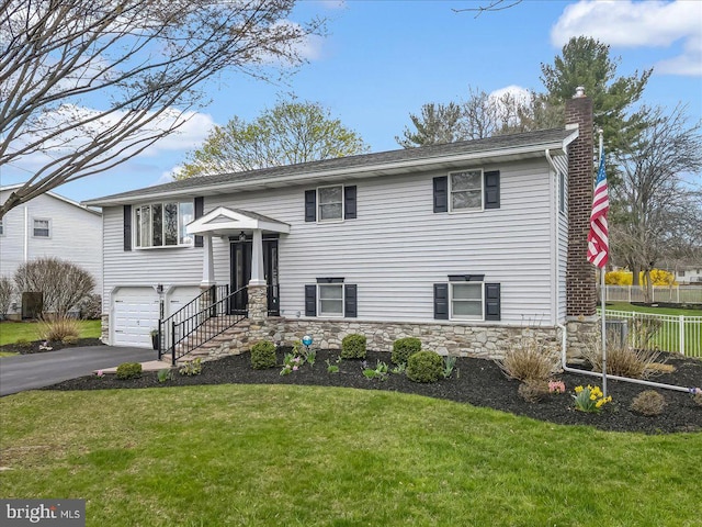 raised ranch featuring a chimney, a garage, driveway, and stone siding