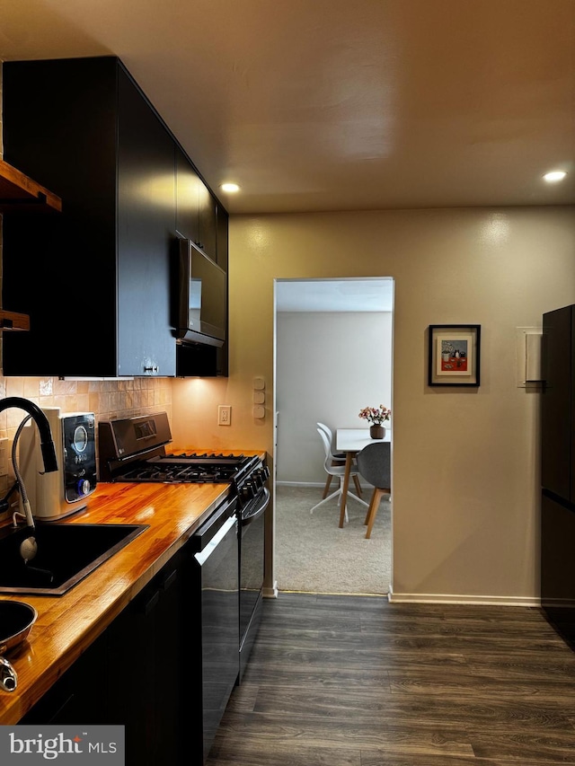 kitchen with wood counters, dark cabinetry, a sink, black range with gas cooktop, and backsplash