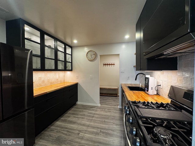 kitchen with stainless steel range with gas stovetop, dark cabinetry, freestanding refrigerator, a sink, and wood counters