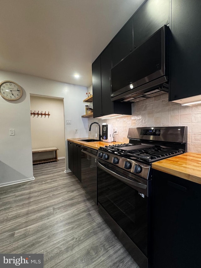 kitchen with stainless steel appliances, dark cabinets, a sink, wood counters, and light wood-style floors