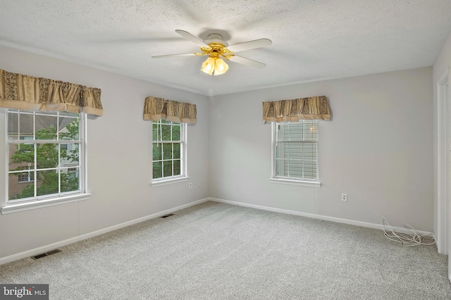spare room featuring carpet, healthy amount of natural light, a ceiling fan, baseboards, and a textured ceiling