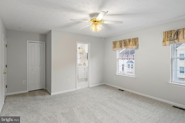 unfurnished bedroom featuring multiple windows, carpet floors, a textured ceiling, baseboards, and a closet