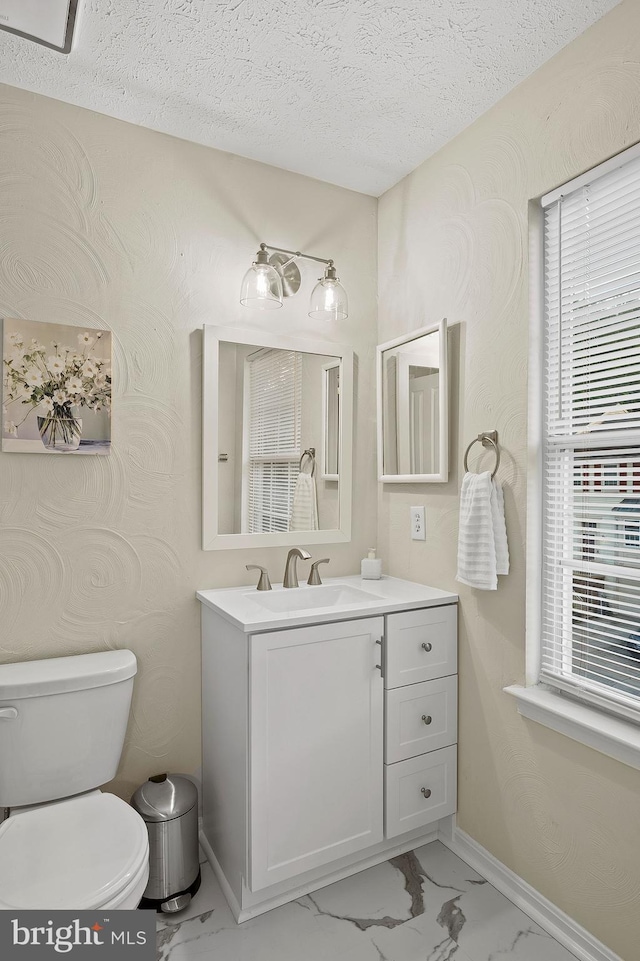 half bathroom with a textured ceiling, toilet, vanity, healthy amount of natural light, and marble look tiles